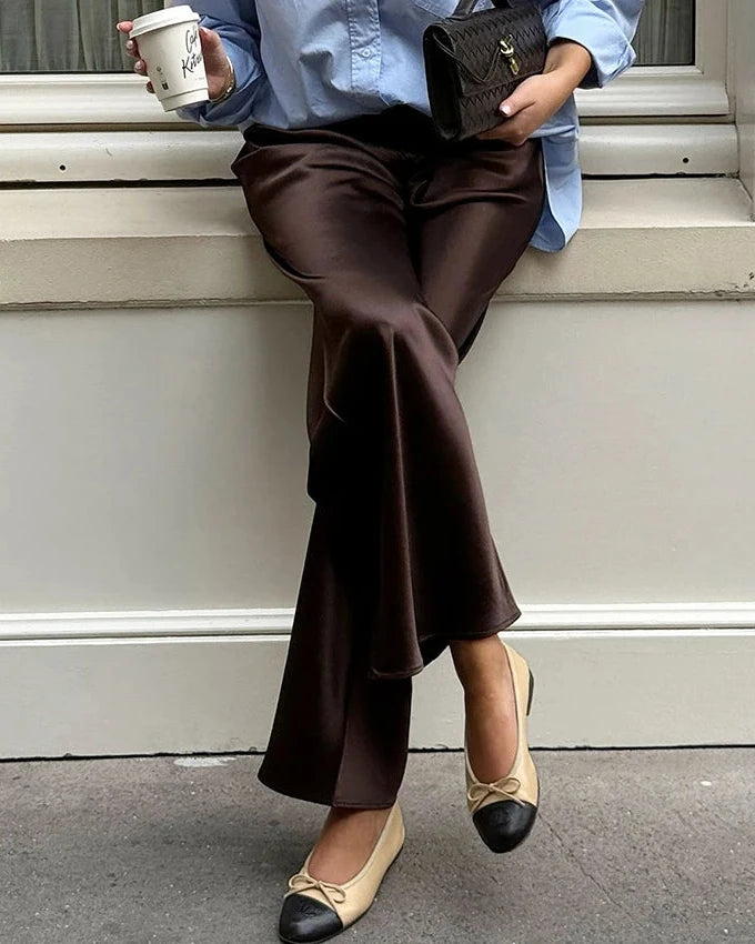 Person sitting on steps wearing brown pants and beige shoes with black accents, holding a coffee cup and wallet.