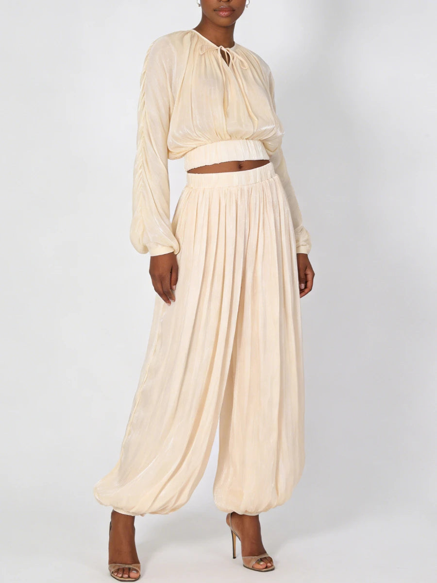 Woman wearing a cream-colored outfit with a top and wide-leg pants on a white background