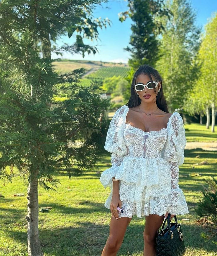 Woman in a white lace dress standing outdoors with greenery in the background